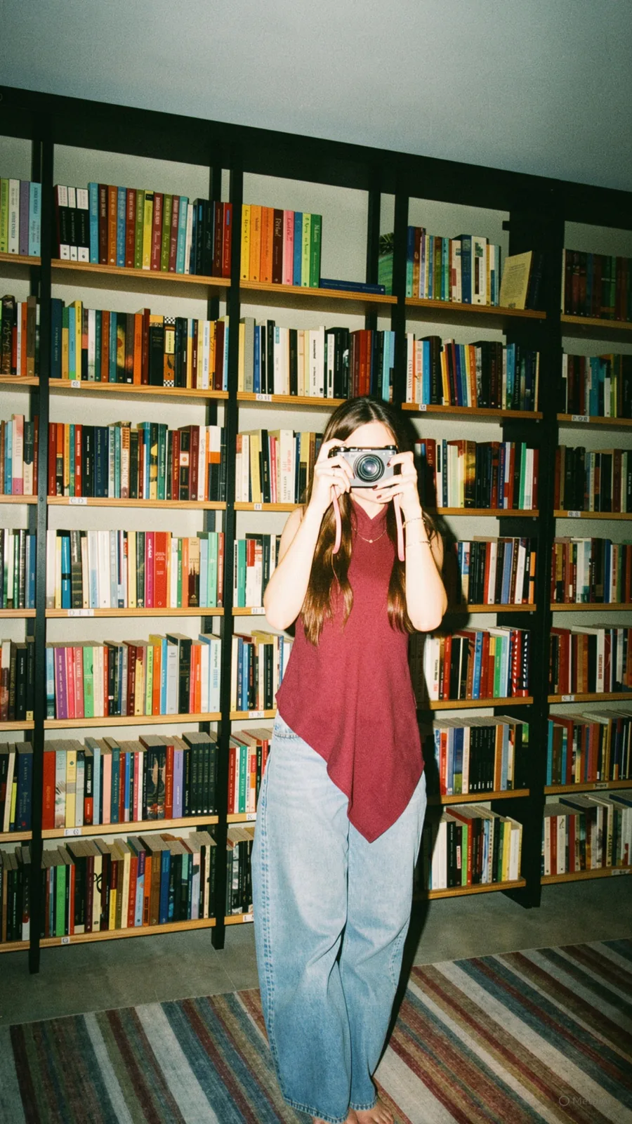 Victória fotografando em frente à estante de livros